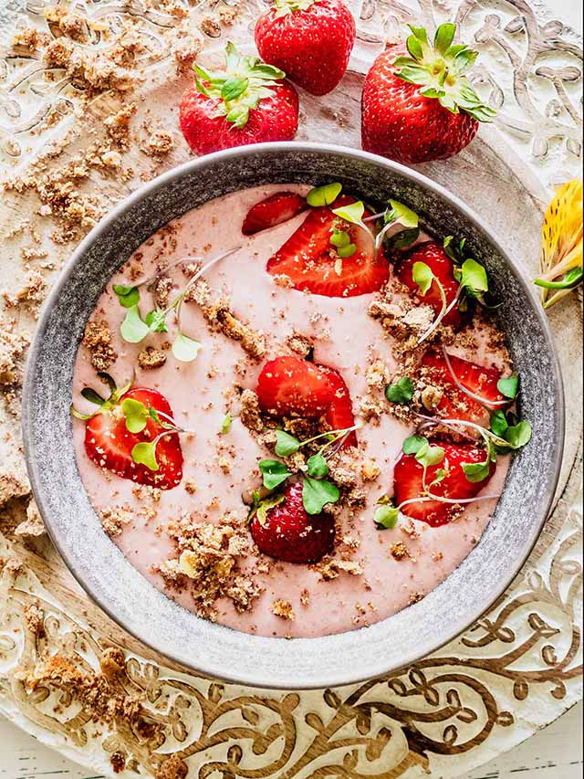 Strawberry banana smoothie bowl topped with fresh strawberries and micro greens
