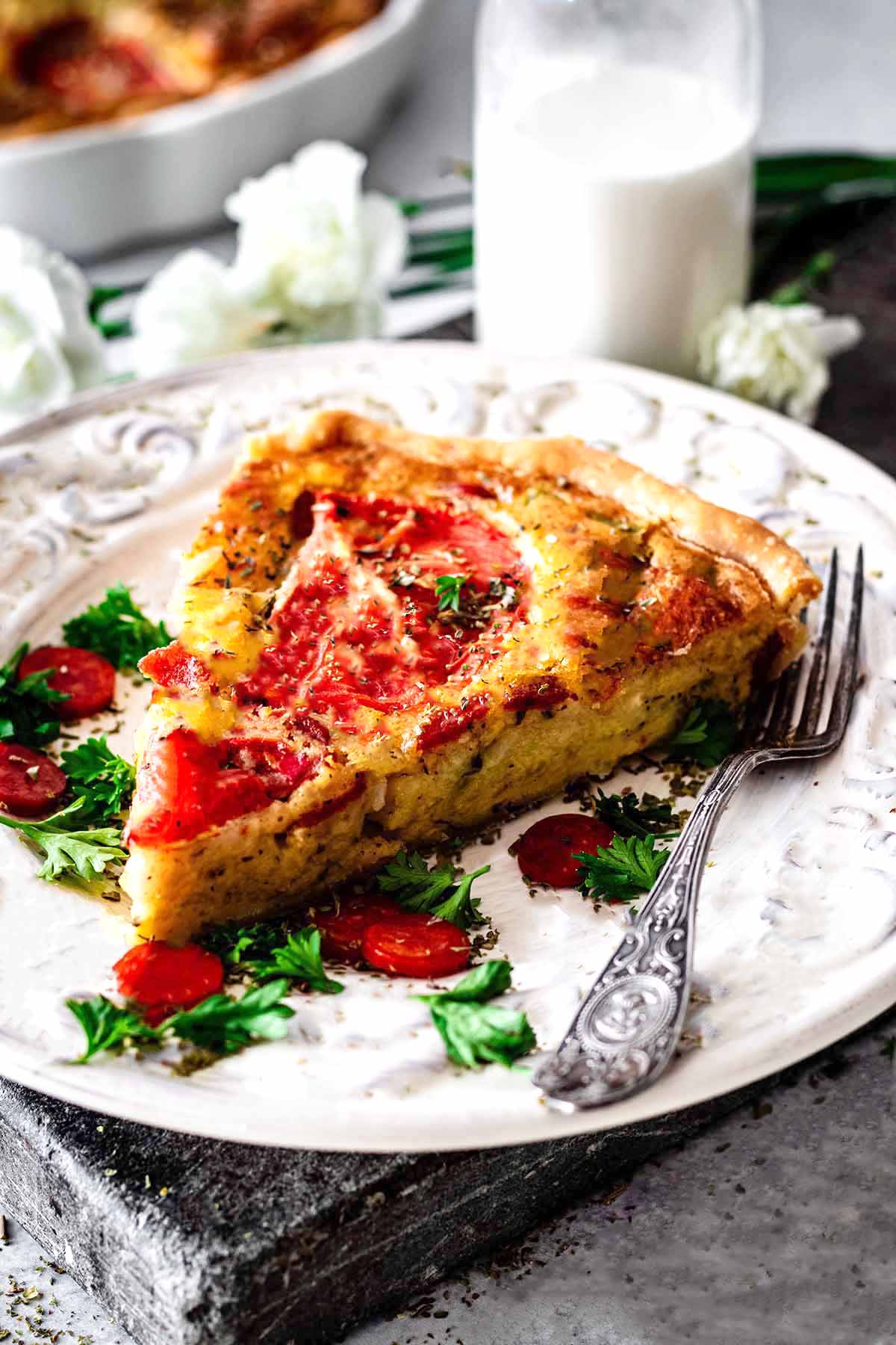 Slice of Italian quiche on a white plate with parsley and mini pepperoni.