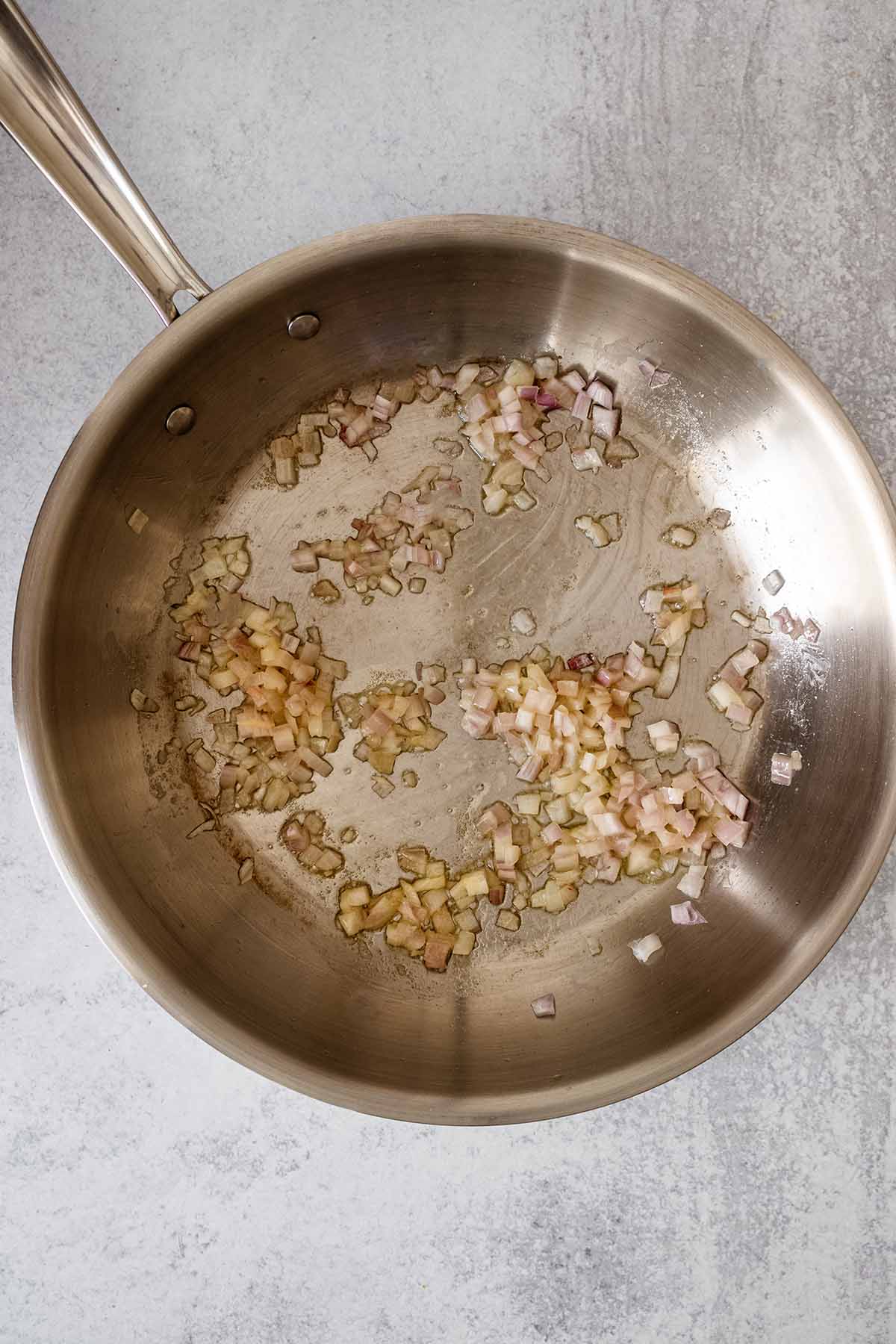 Chopped shallot cooking in a stainless steel skillet,