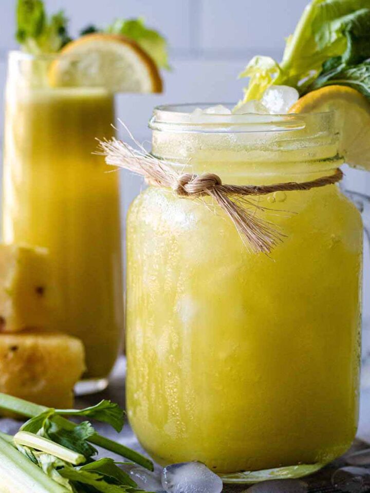 Pineapple celery juice in a jar mug garnished with celery greens, fresh mint, and a lemon slice.