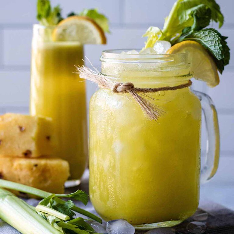 Pineapple celery juice in a jar mug garnished with celery greens, fresh mint, and a lemon slice.