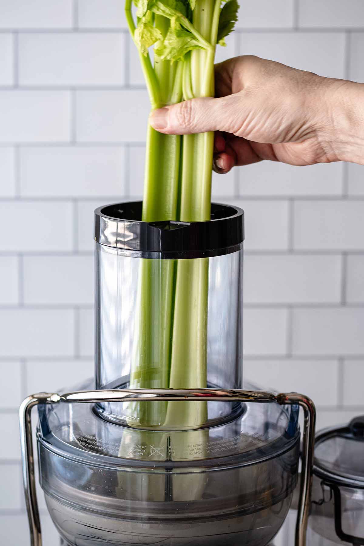 Celery stalks being added to the chute of a juice extractor.