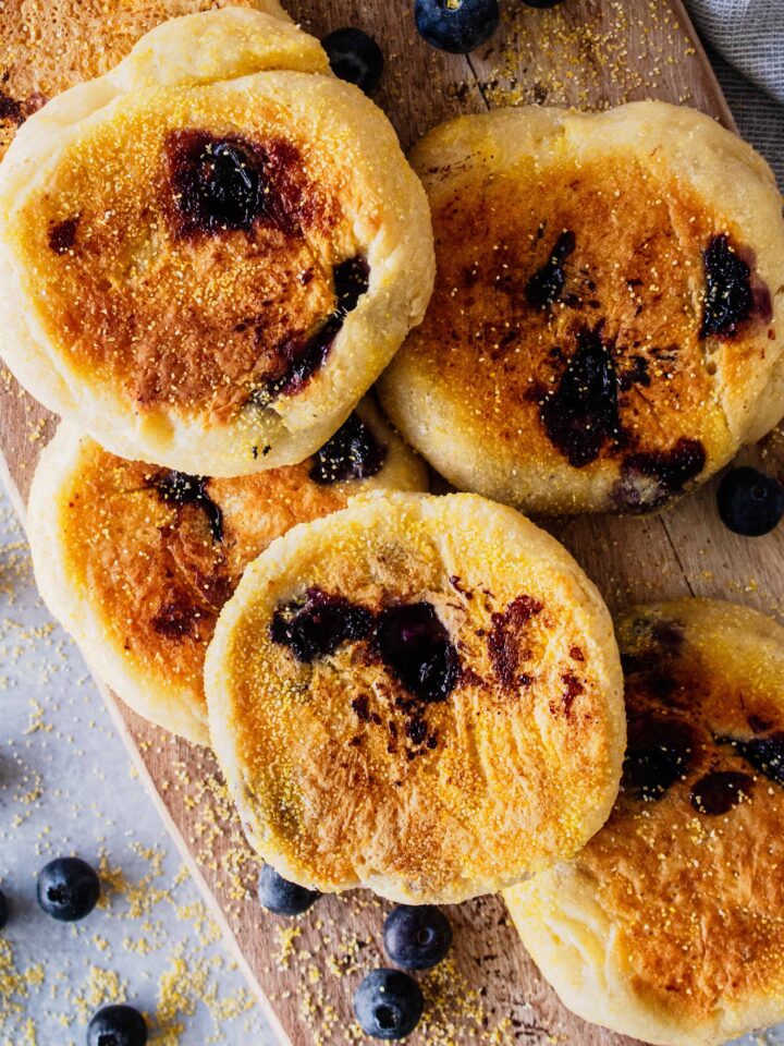 Overhead view of a stack of blueberry English muffins on a wooden cutting board.