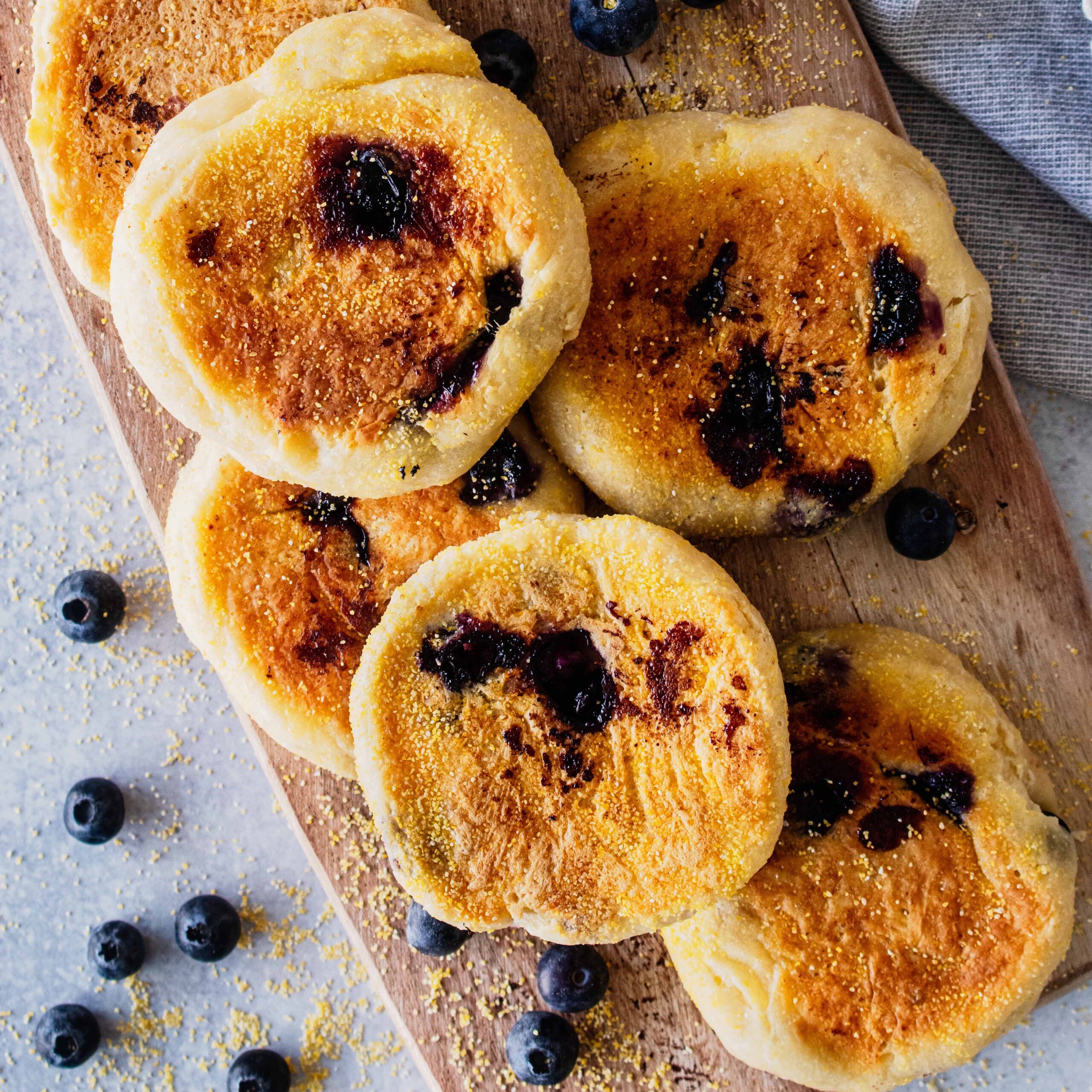 Overhead view of a stack of blueberry English muffins on a wooden cutting board.