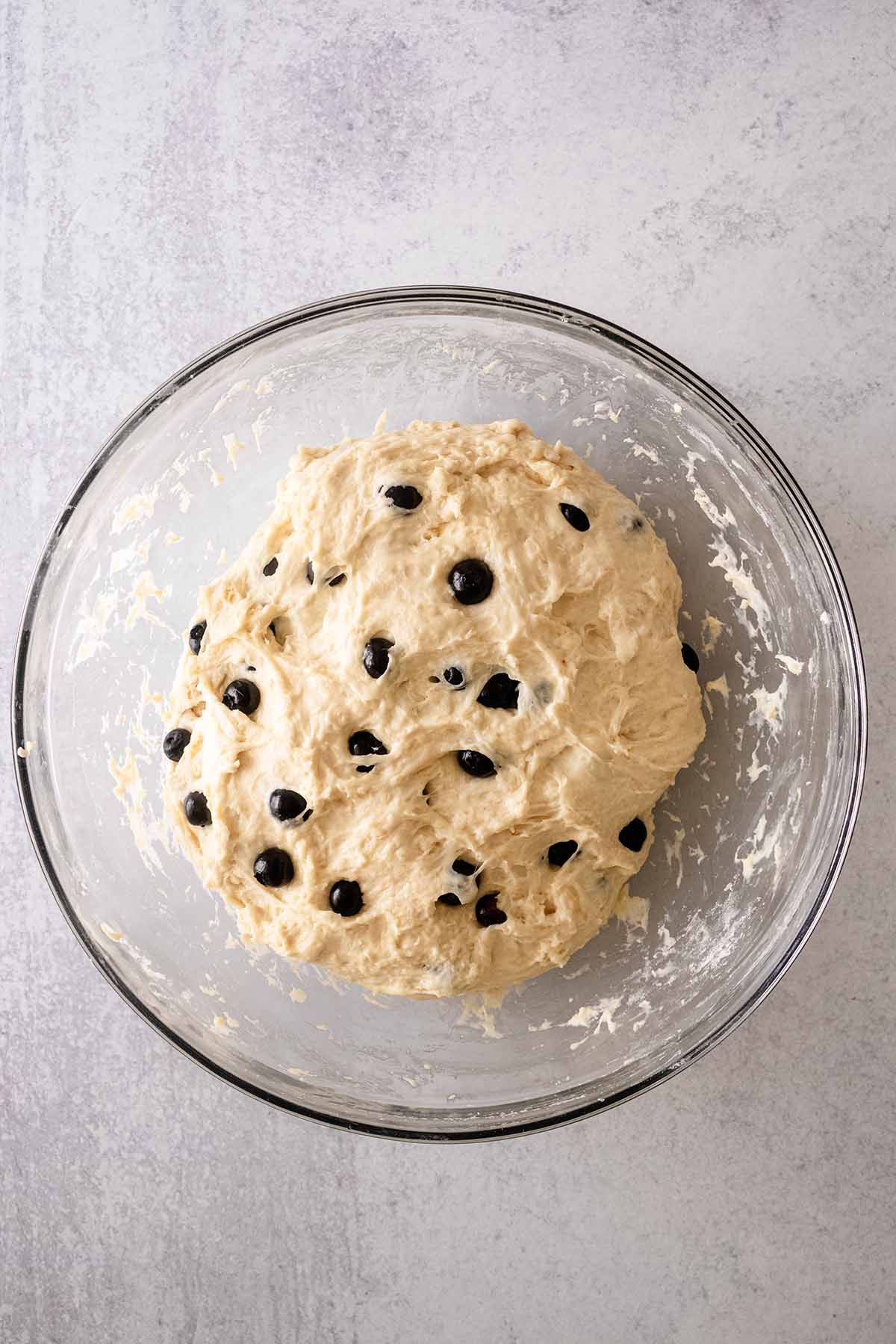 Blueberry English muffin dough in a glass bowl.