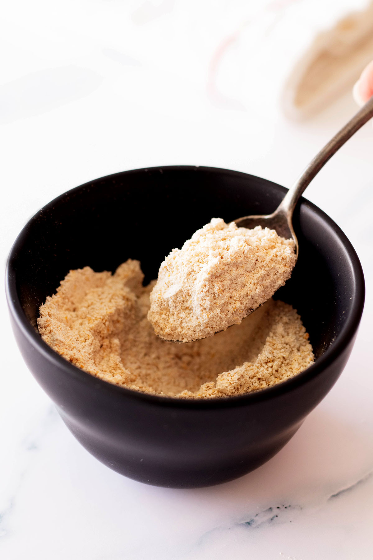 Oat flour in a small black bowl with a spoon.