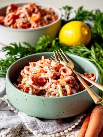Carrot cucumber salad in a green bowl with two gold forks.