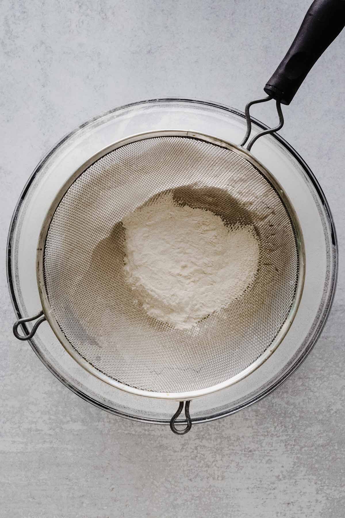 Dry ingredients in a mesh strainer over a large glass bowl.