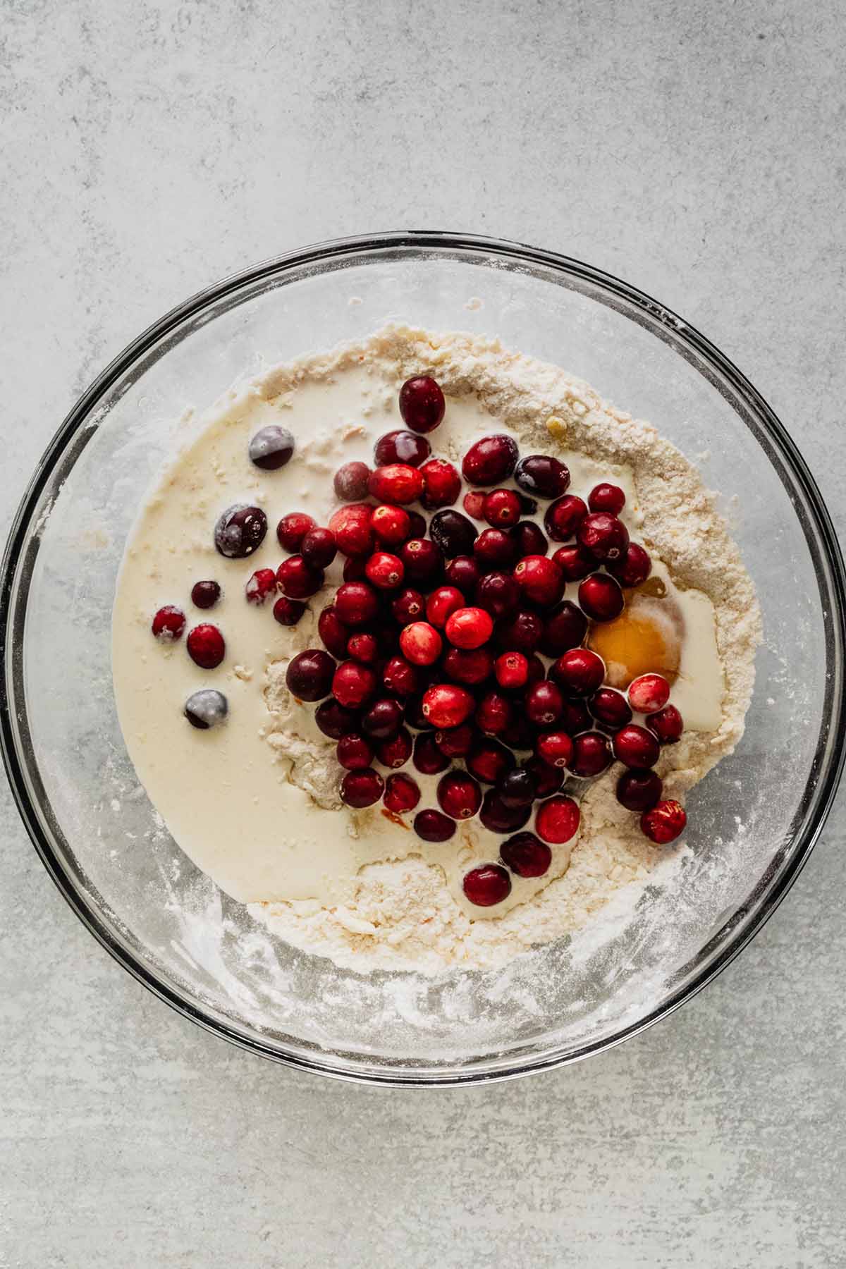 Wet ingredients and cranberries in a glass bowl with crumbly dry mixture.