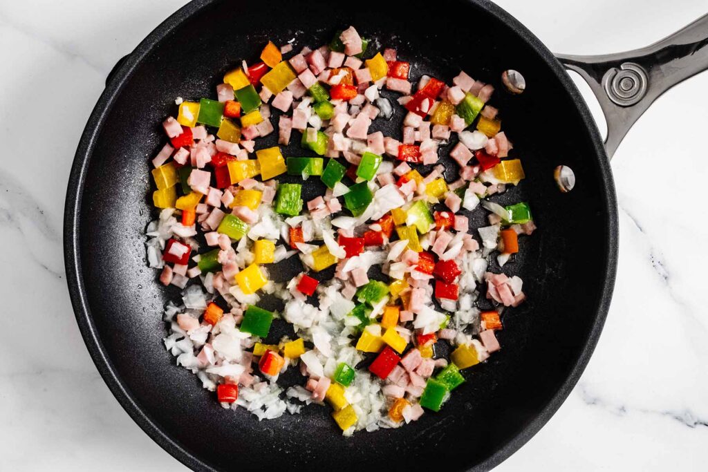 Chopped onion, ham, and bell peppers cooking in a skillet.