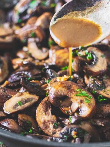 Sauce from the skillet being spooned over sautéed garlic butter mushrooms as they sit in the skillet.