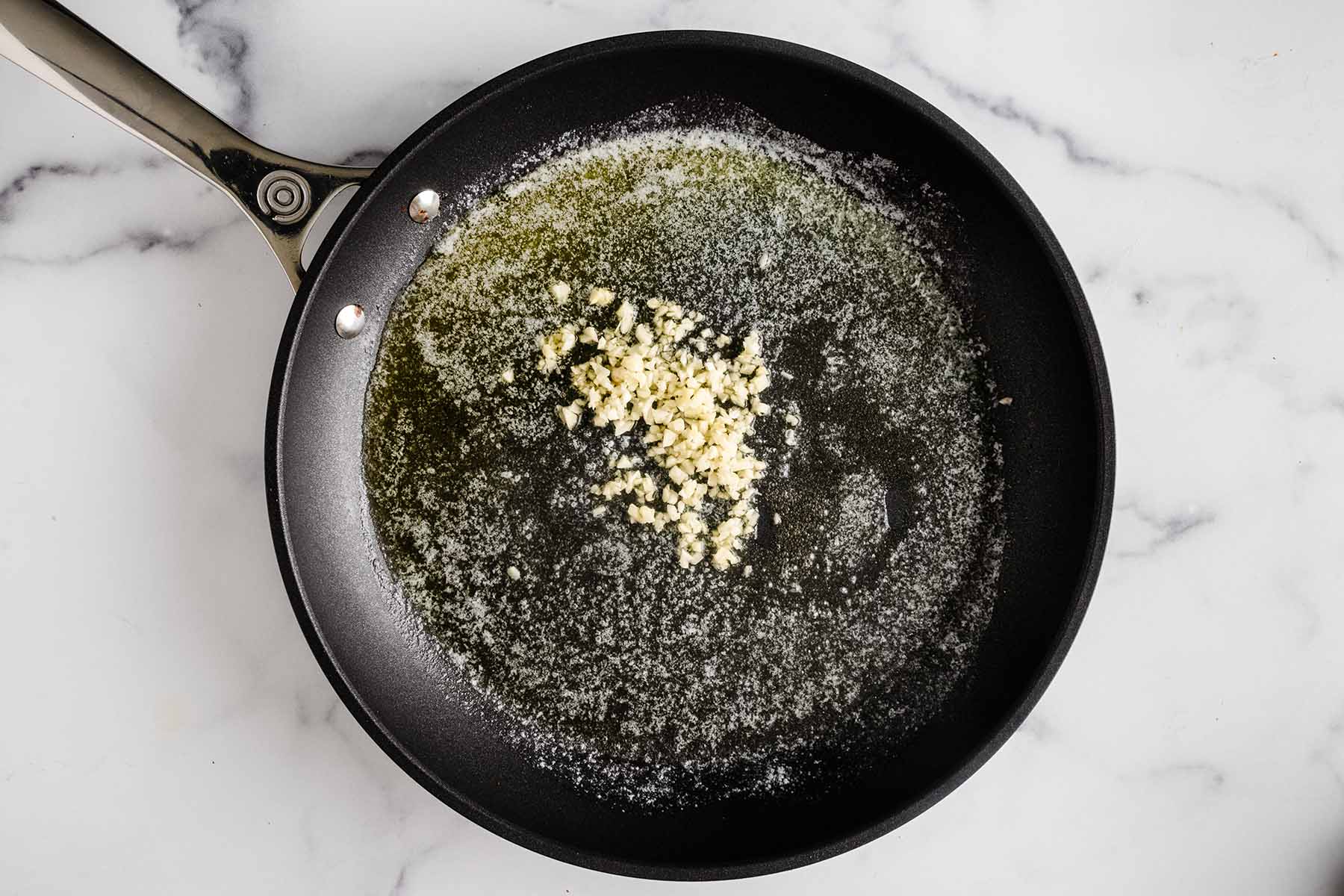Minced garlic added to melted butter in a skillet.