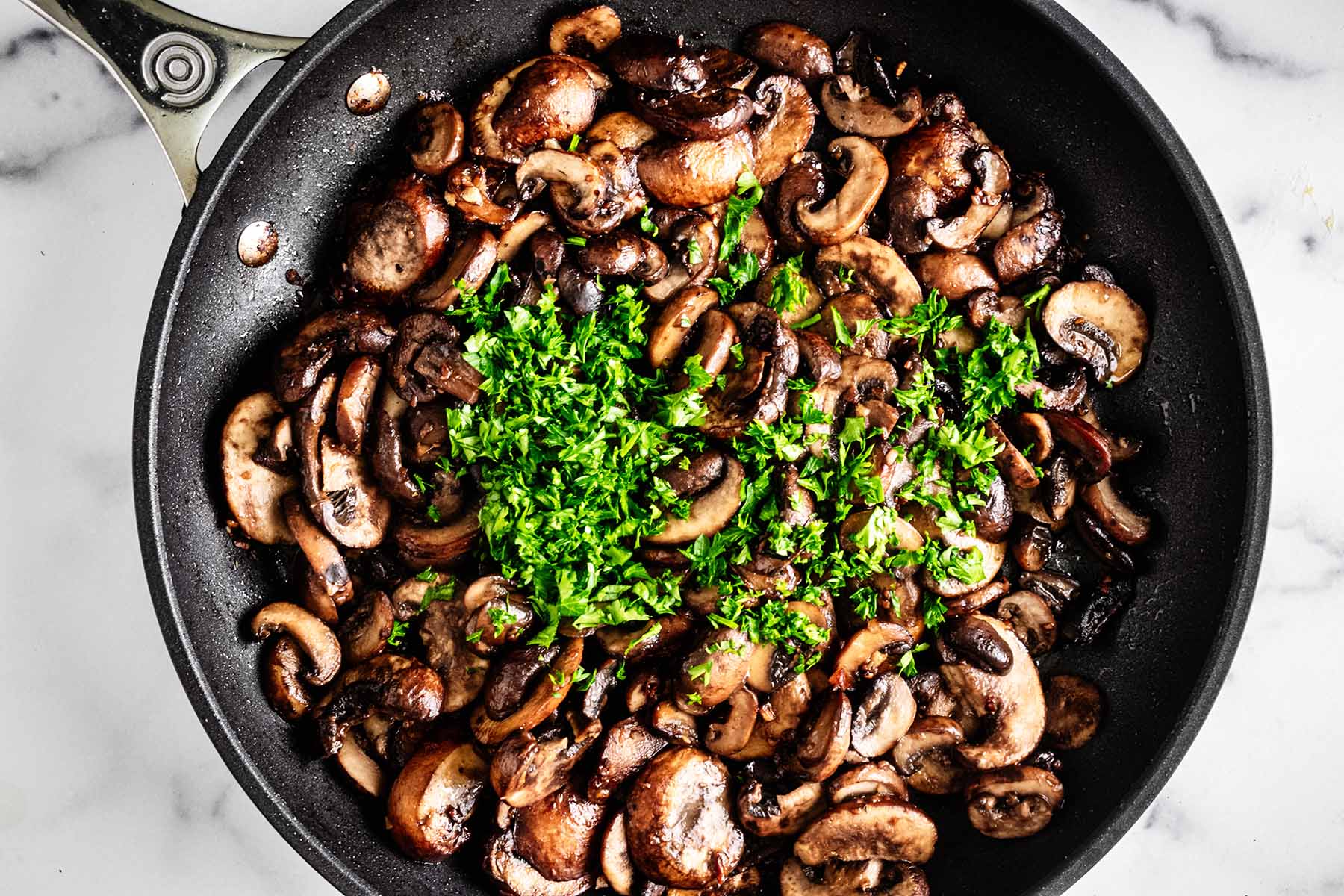 Closeup of chopped parsley added to skillet with sautéed mushrooms.