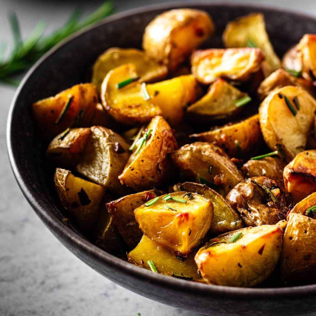 Close up of garlic rosemary roasted potatoes in a dark grey bowl.