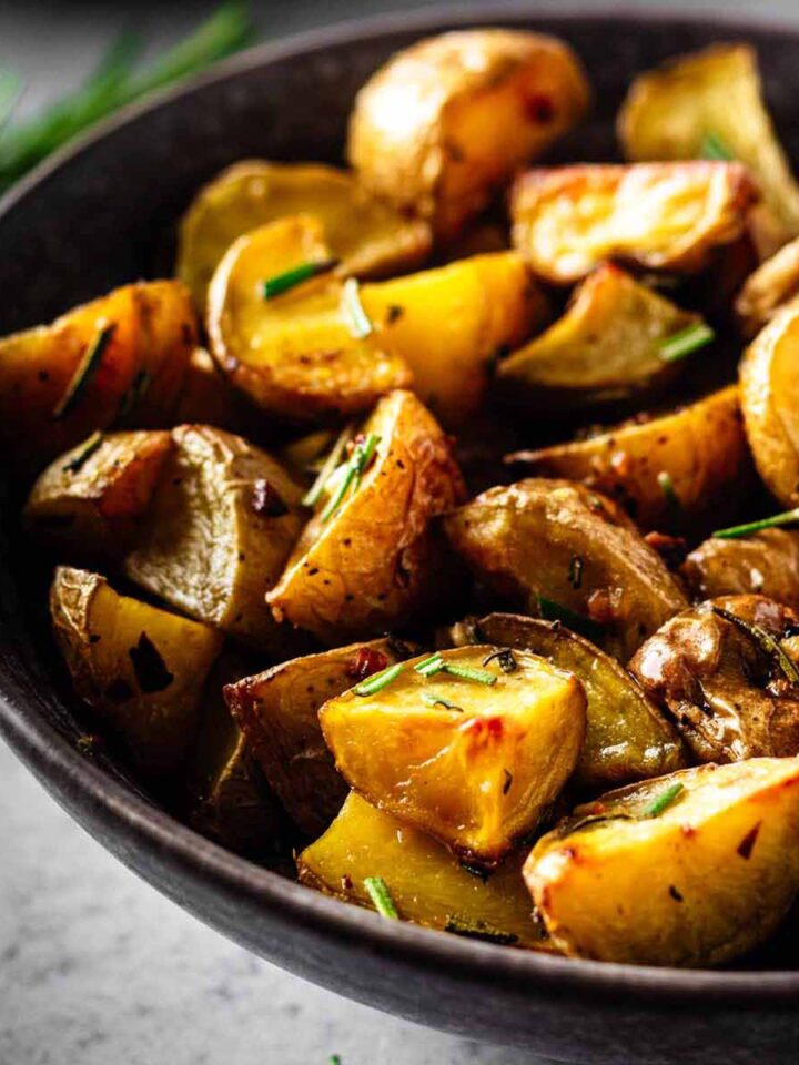 Close up of garlic rosemary roasted potatoes in a dark grey bowl.