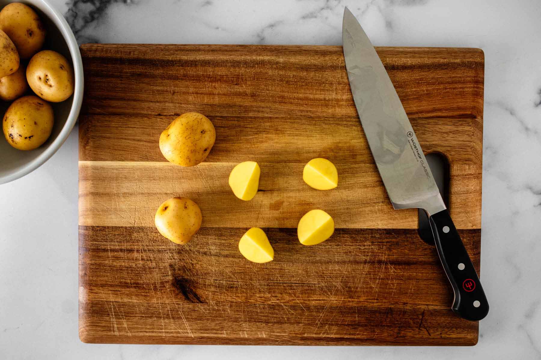 Potatoes being chopped with a chef's knife on a wooden cutting board.