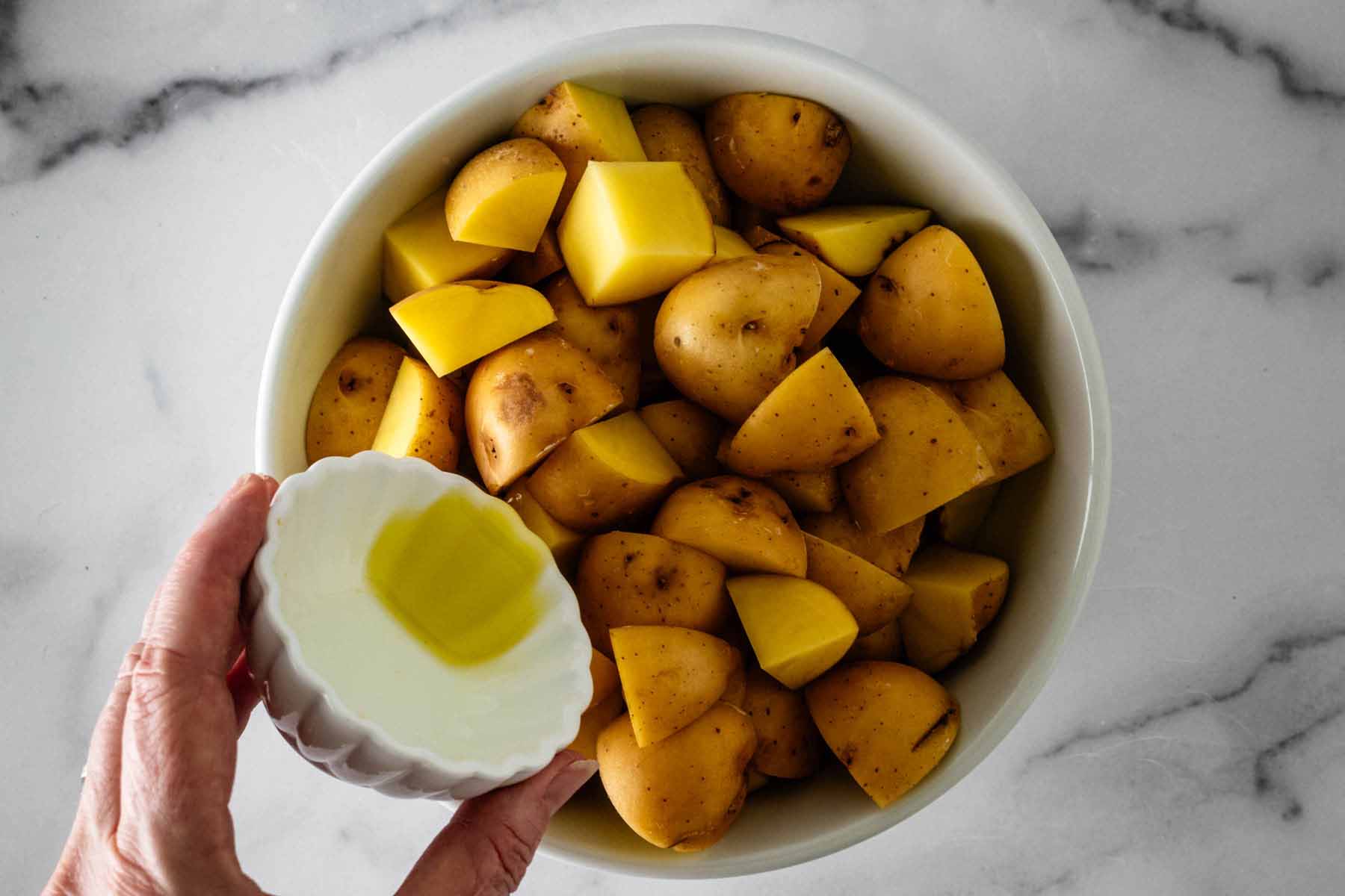 Olive oil is poured into a bowl of chopped golden potatoes