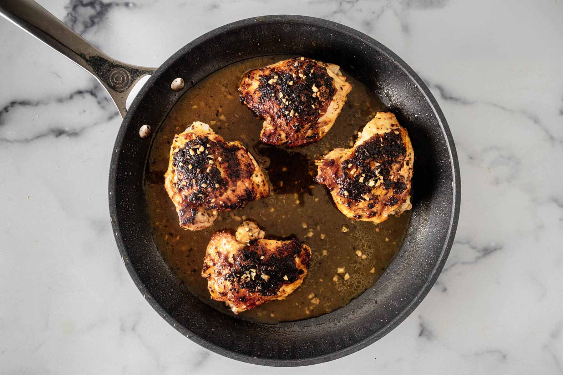 Four chicken thighs resting in the pan sauce in the hot skillet.