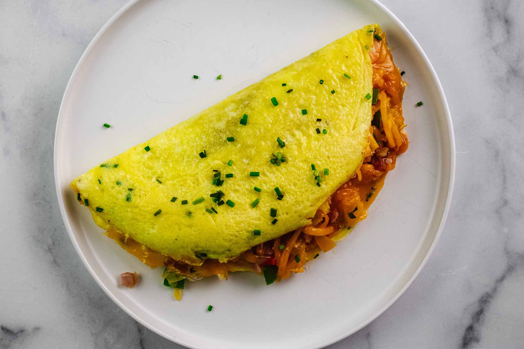 Western omelette folded over itself into a half moon shape and served on a white plate.