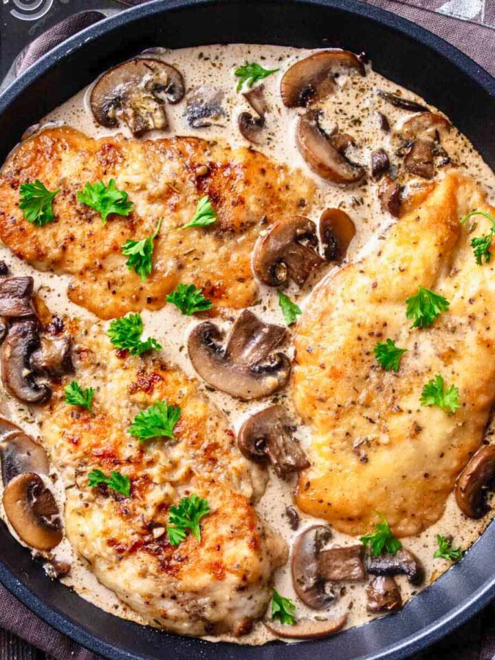 Closeup overhead view of three cooked chicken cutlets in mushroom sauce in a large skillet