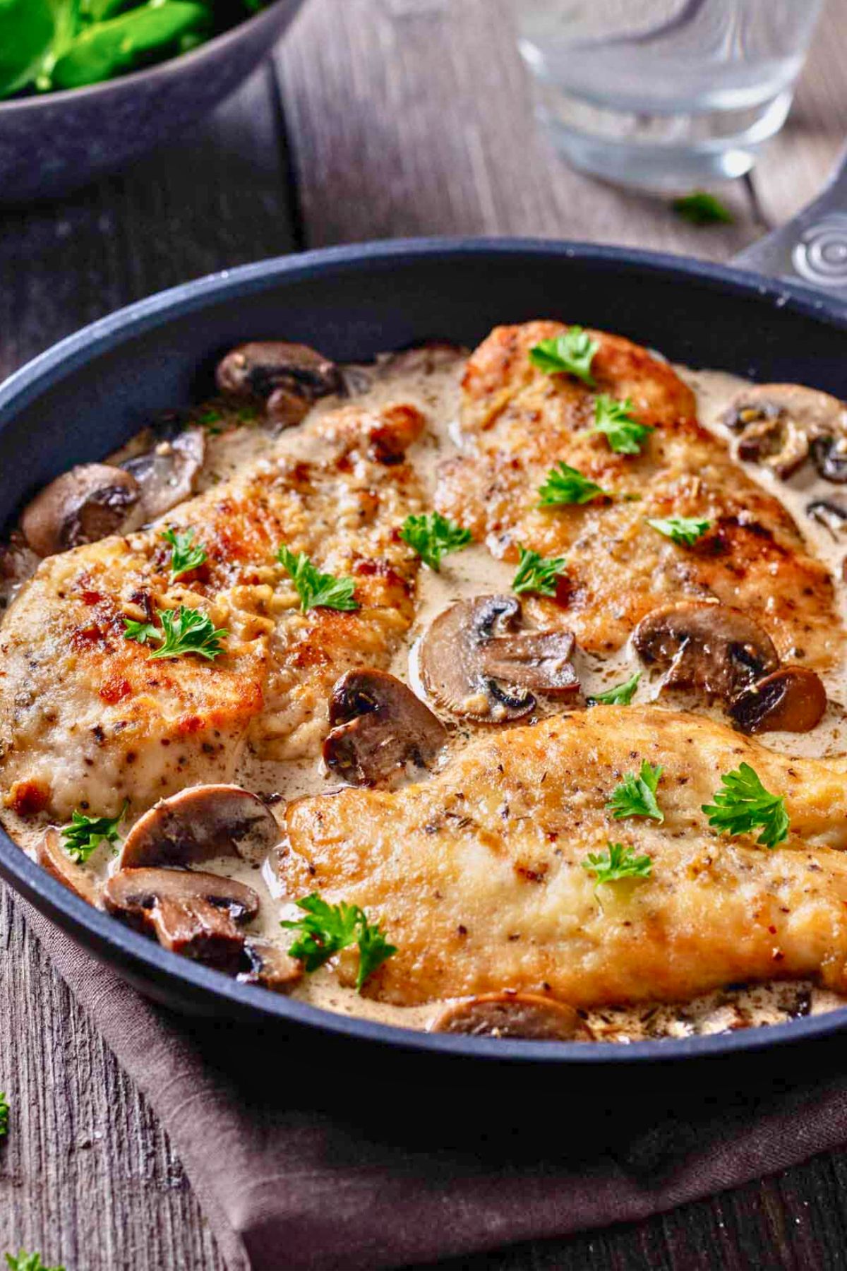 Front view of three cooked chicken cutlets in mushroom sauce in a large skillet.