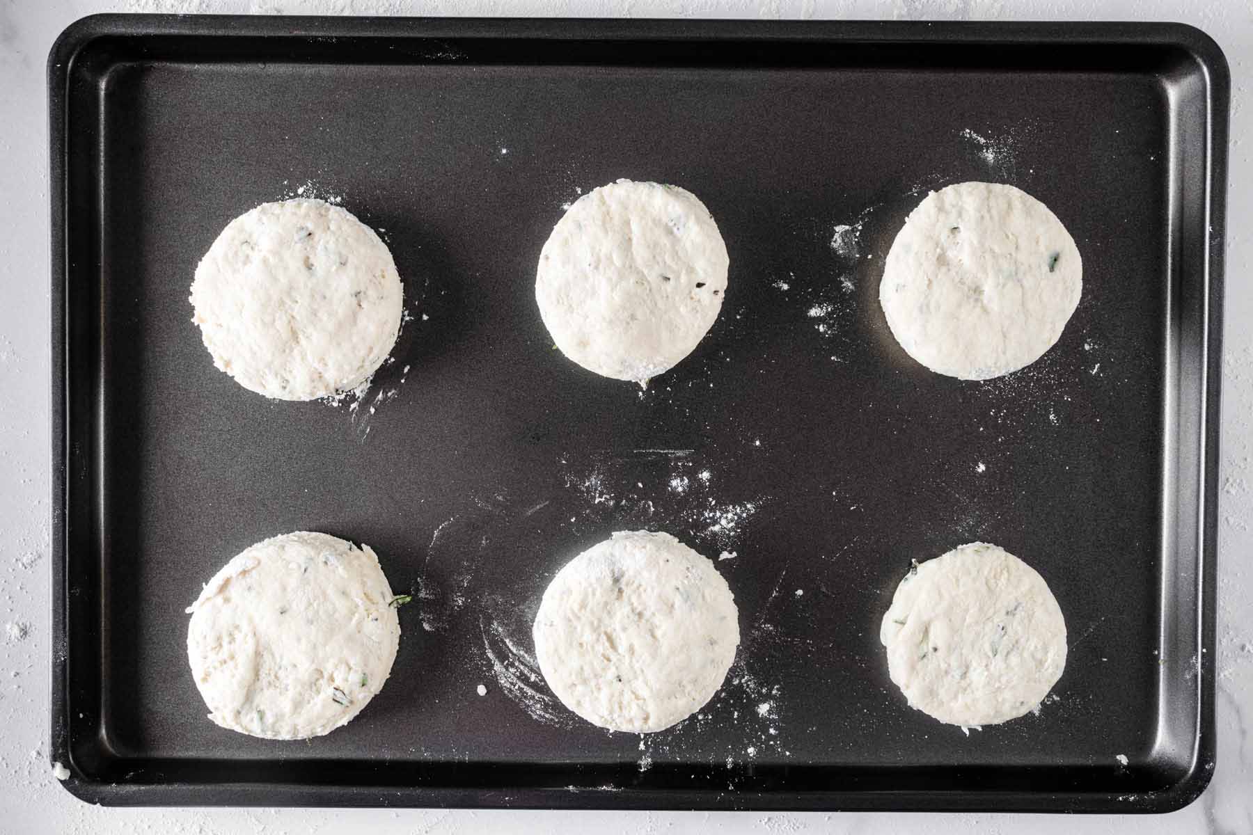 Six unbaked biscuits laid out onto a baking sheet.