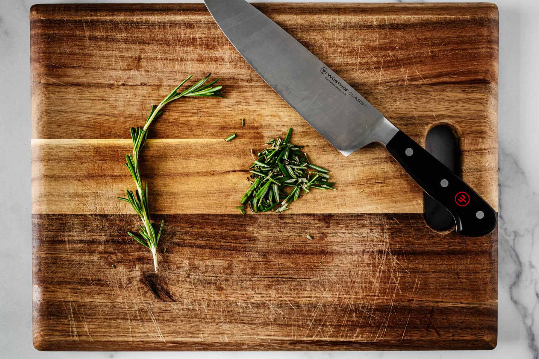 Chopped rosemary on a cutting board with a chef's knife.