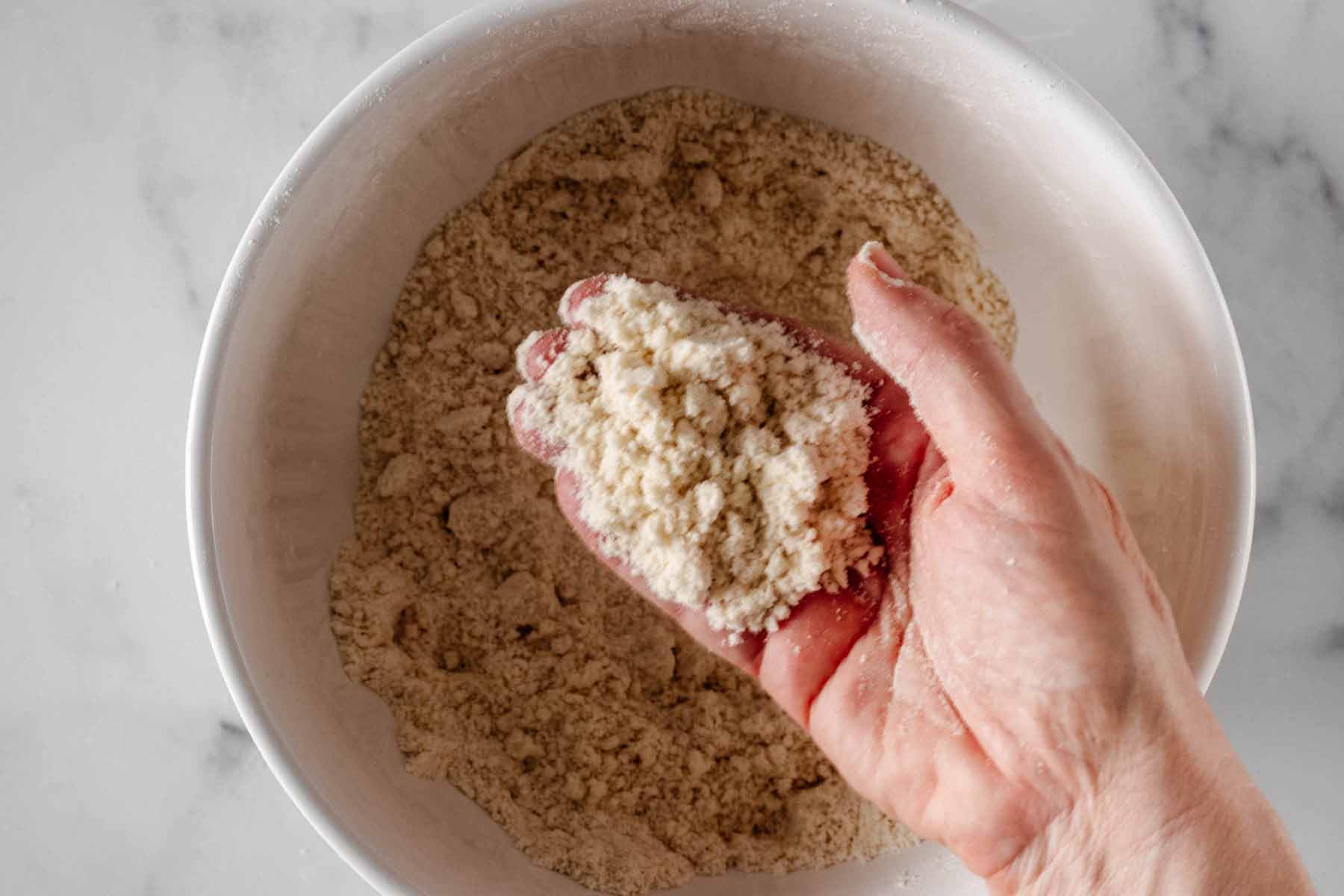 A hand holding a handful of flour and butter mixture to demonstrate the texture of the mixture.