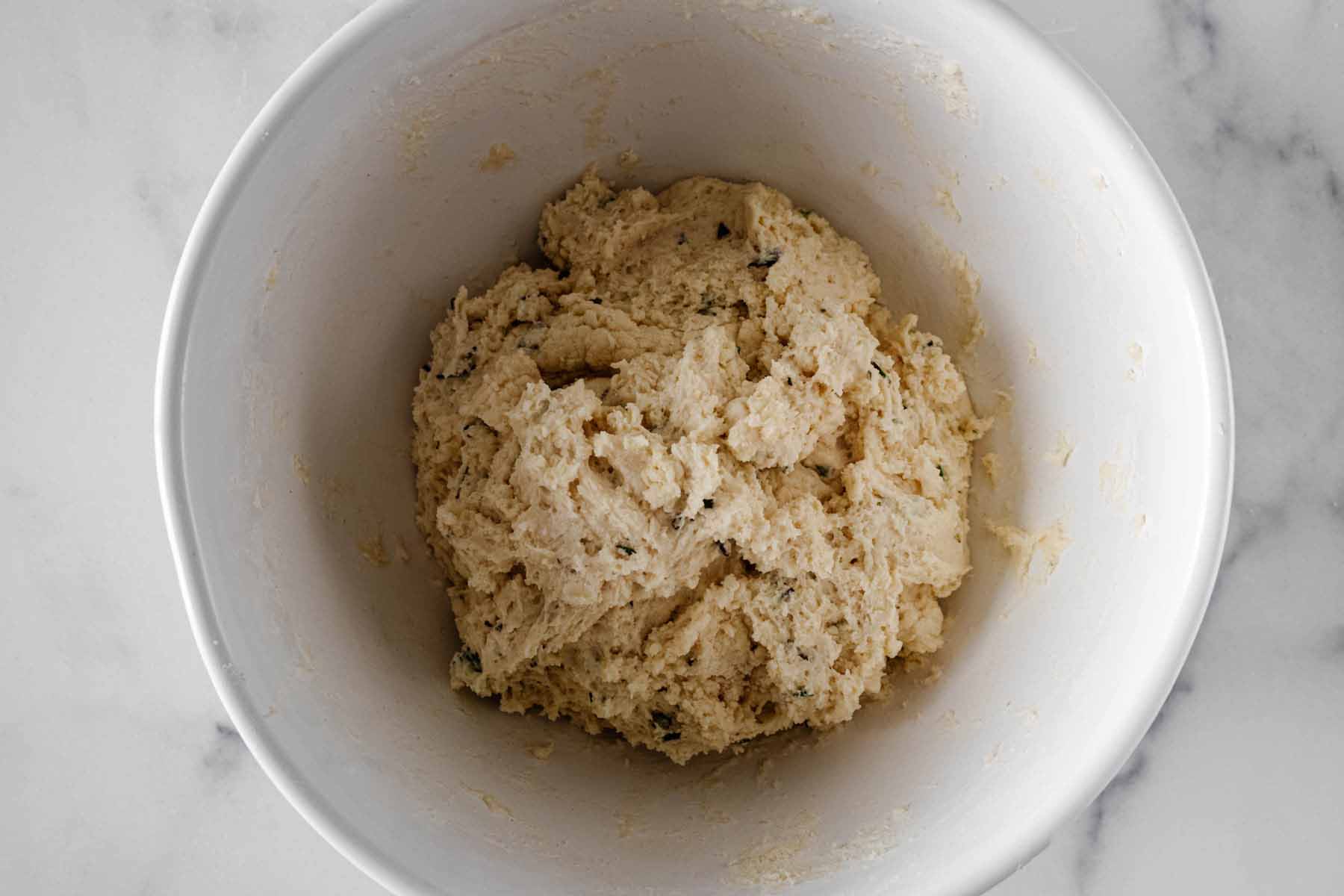 Rosemary biscuit dough in a white bowl.