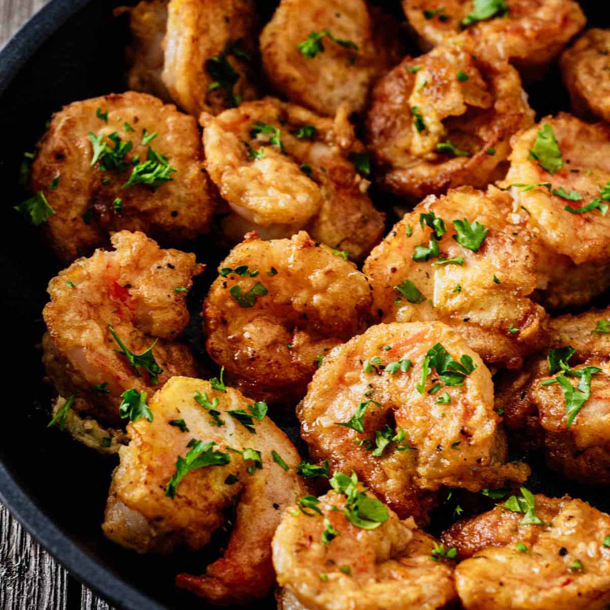 Tight close up of shrimp Francese garnished with chopped parsley in a skillet.