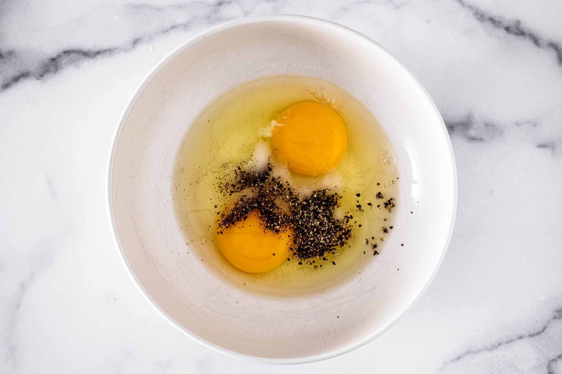 Raw eggs, salt, and pepper in a white bowl.