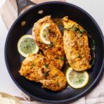 Overhe4ad close up of three chicken limone cutlets topped with fresh thyme leaves in a skillet with sliced lemons