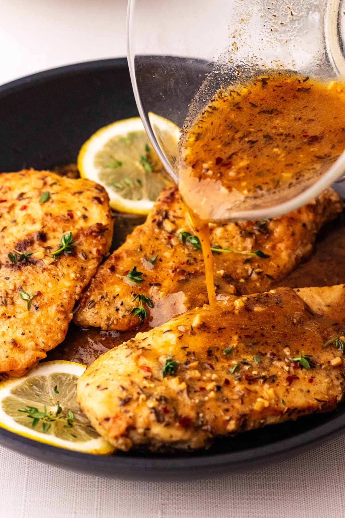 Three chicken limone cutlets topped with fresh thyme leaves in a skillet with sauce being poured over the top