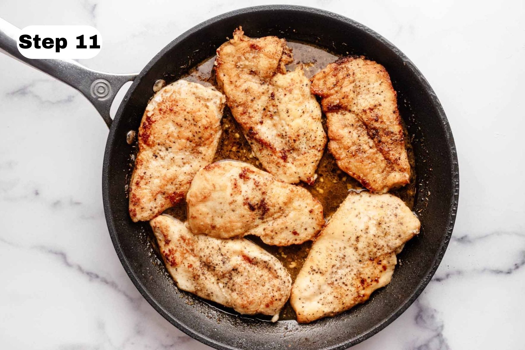 Six chicken breast cutlets in a large skillet with lemon sauce.