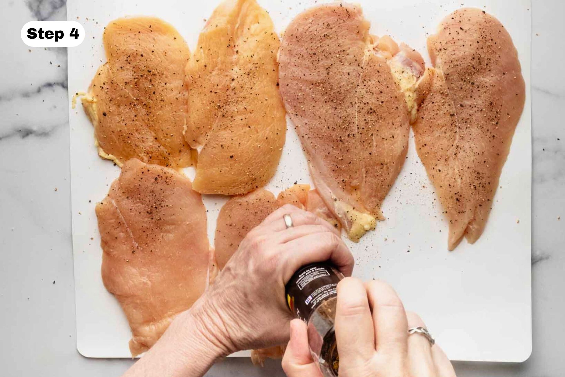 Six chicken breast cutlets being seasoned with salt and pepper.