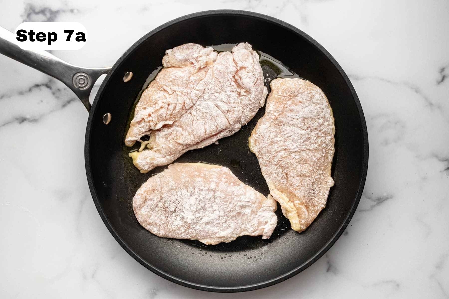 Three uncooked chicken breast cutlets in a large skillet.
