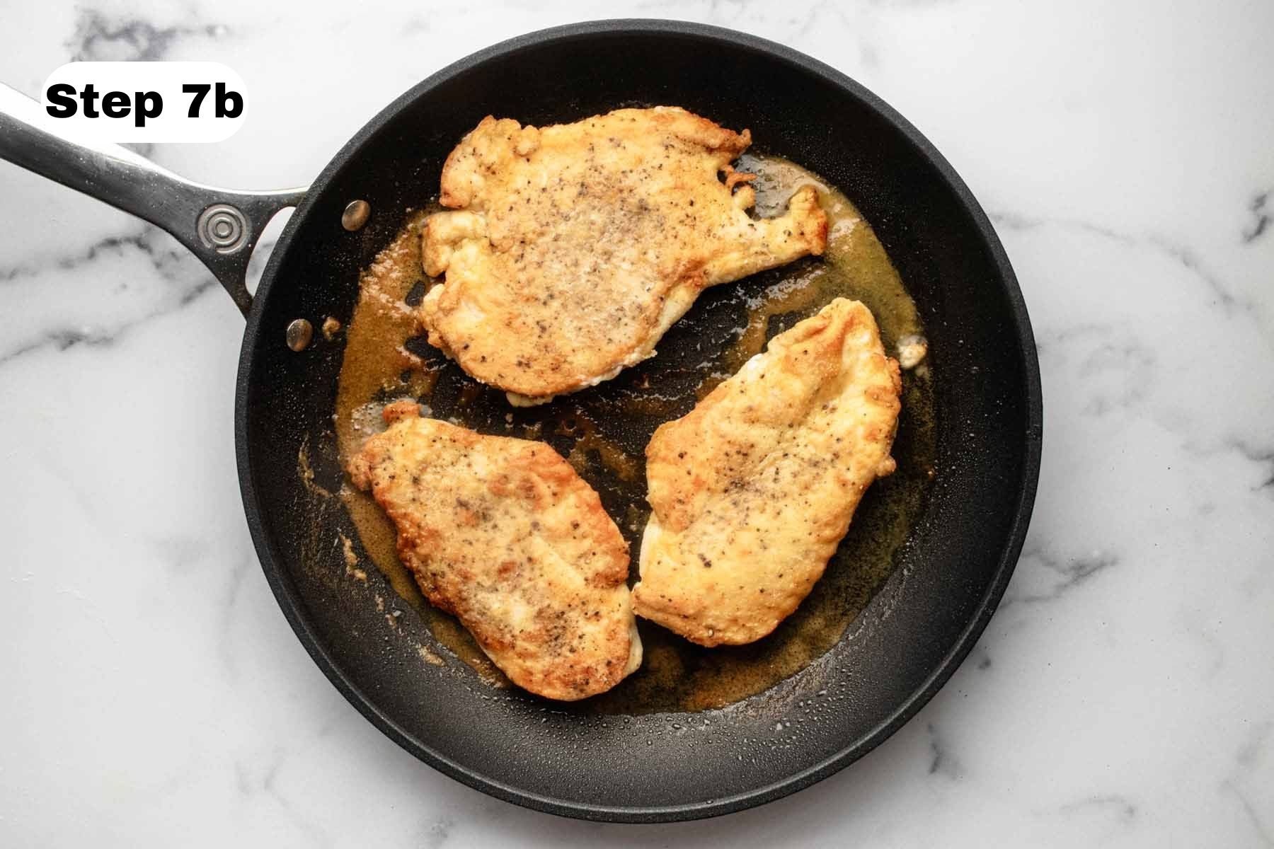 Three cooked chicken cutlets in a large skillet.