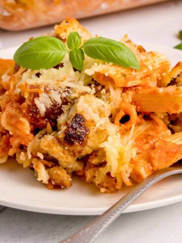 Serving of chicken Parmesan casserole garnished with basil leaves on a white plate with a fork.