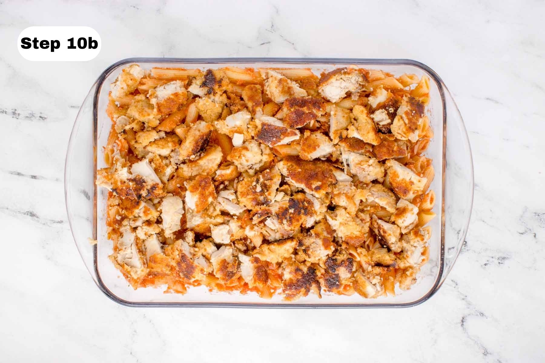 Cooked chicken thigh pieces layered on top of pasta in a glass baking dish.