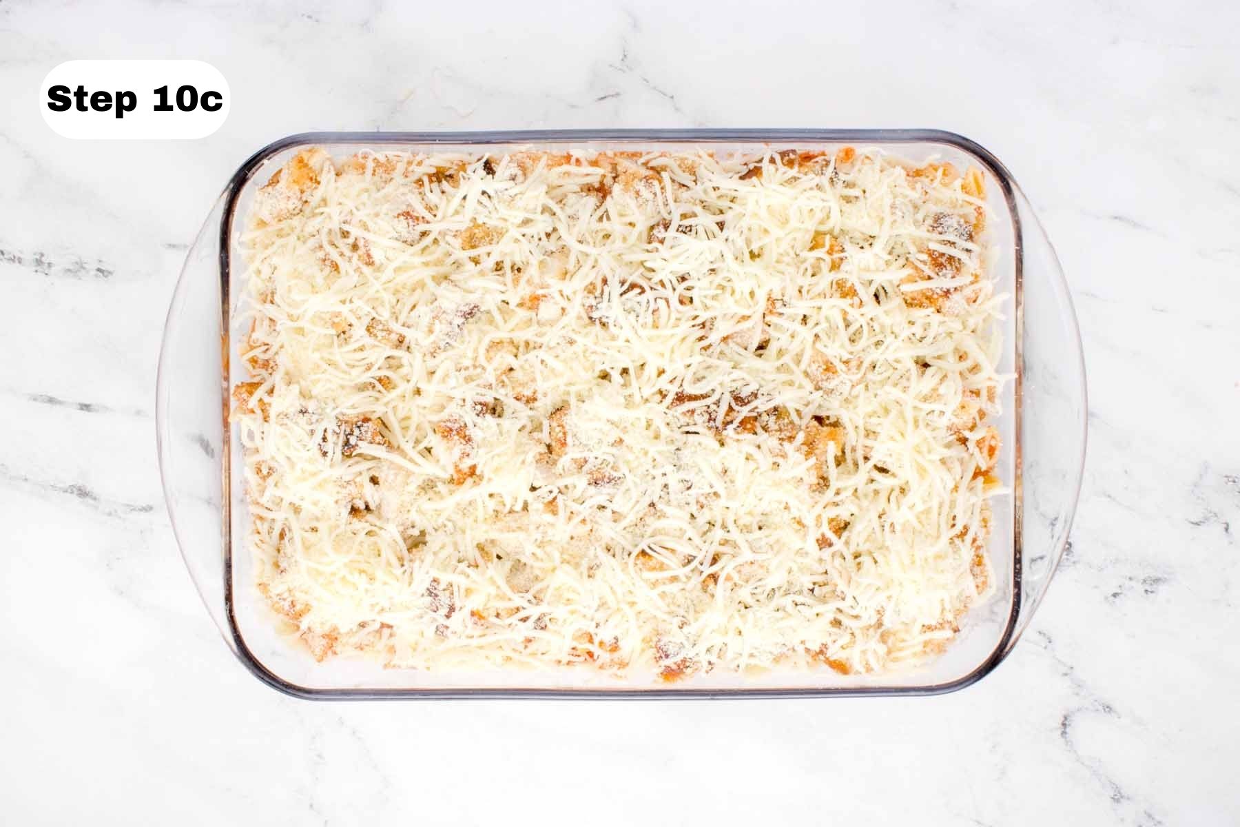 Shredded mozzarella and Parmesan layered on top of cooked chicken thigh pieces in a glass baking dish.