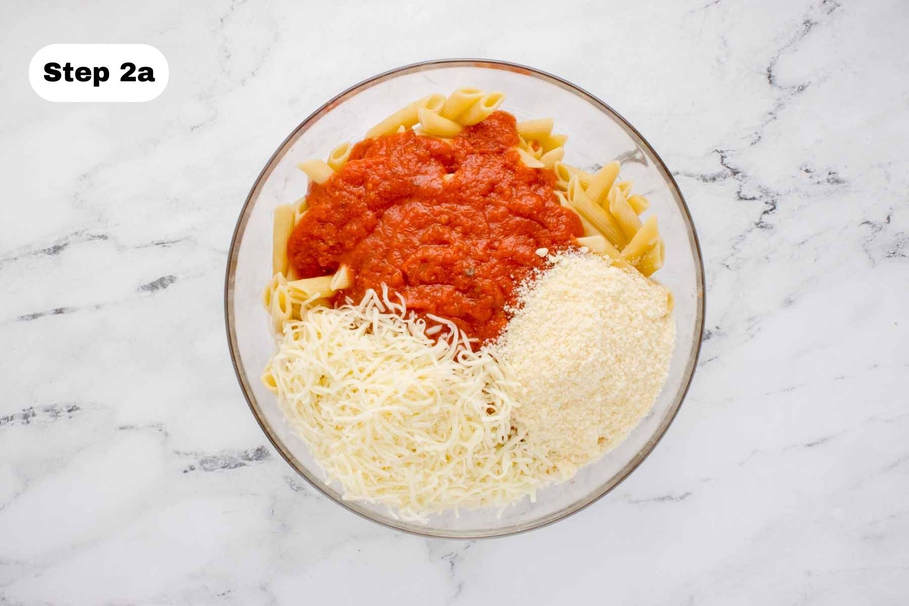 Cooked penne pasta, marinara sauce, mozzarella, and Parmesan in a glass bowl.