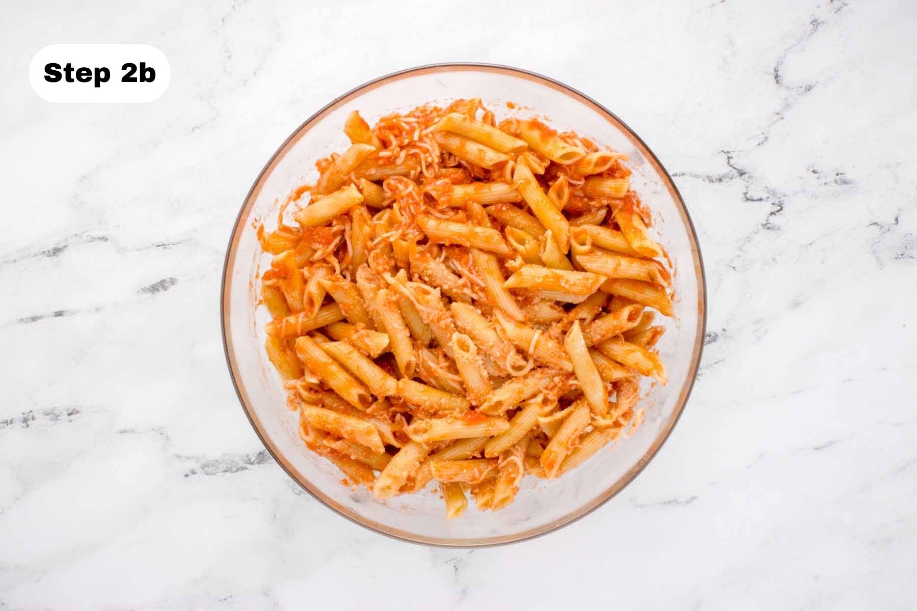 Cooked penne pasta combined with marinara and cheeses in a glass bowl.