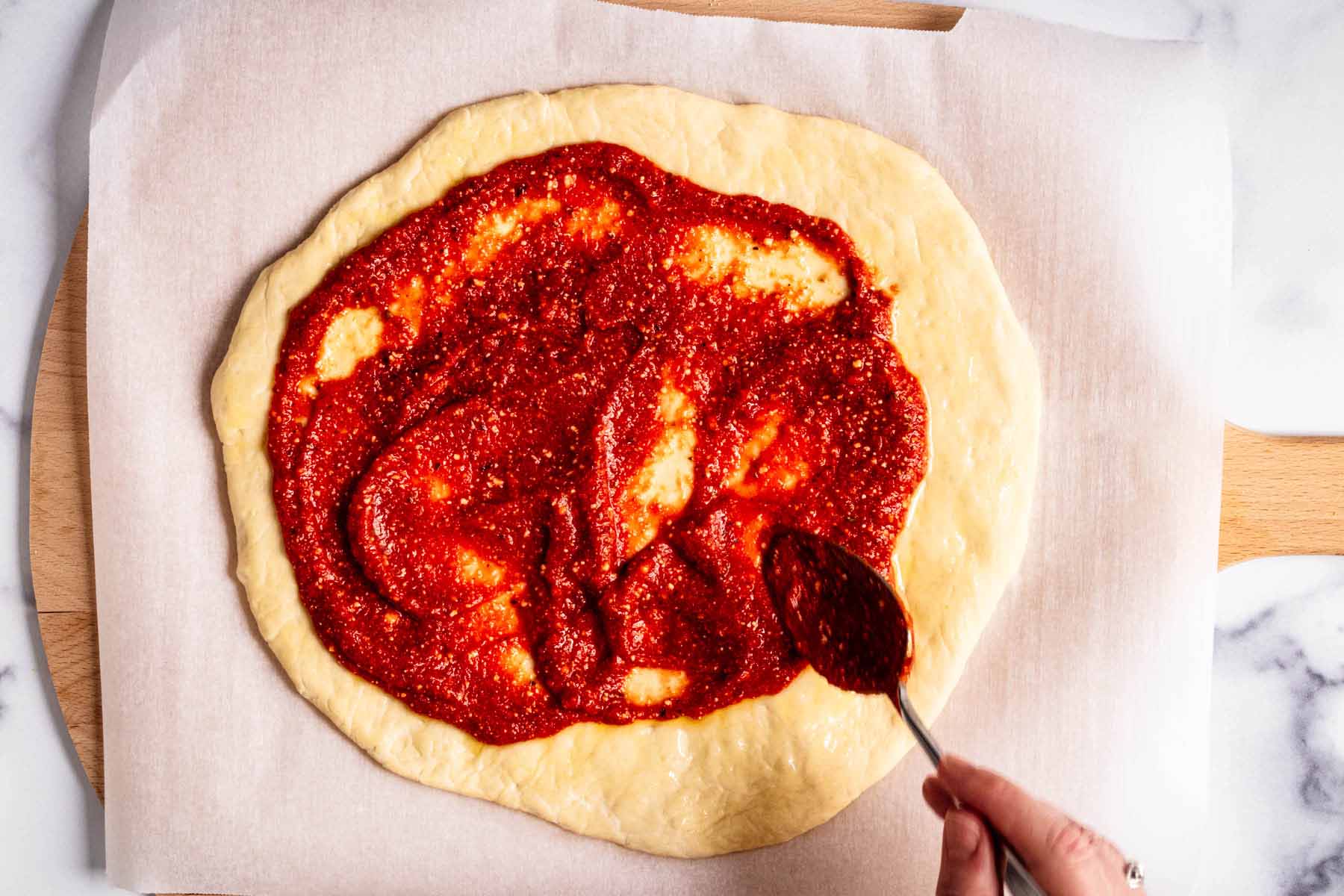 Pizza sauce being spread with a spoon onto unbaked pizza crust