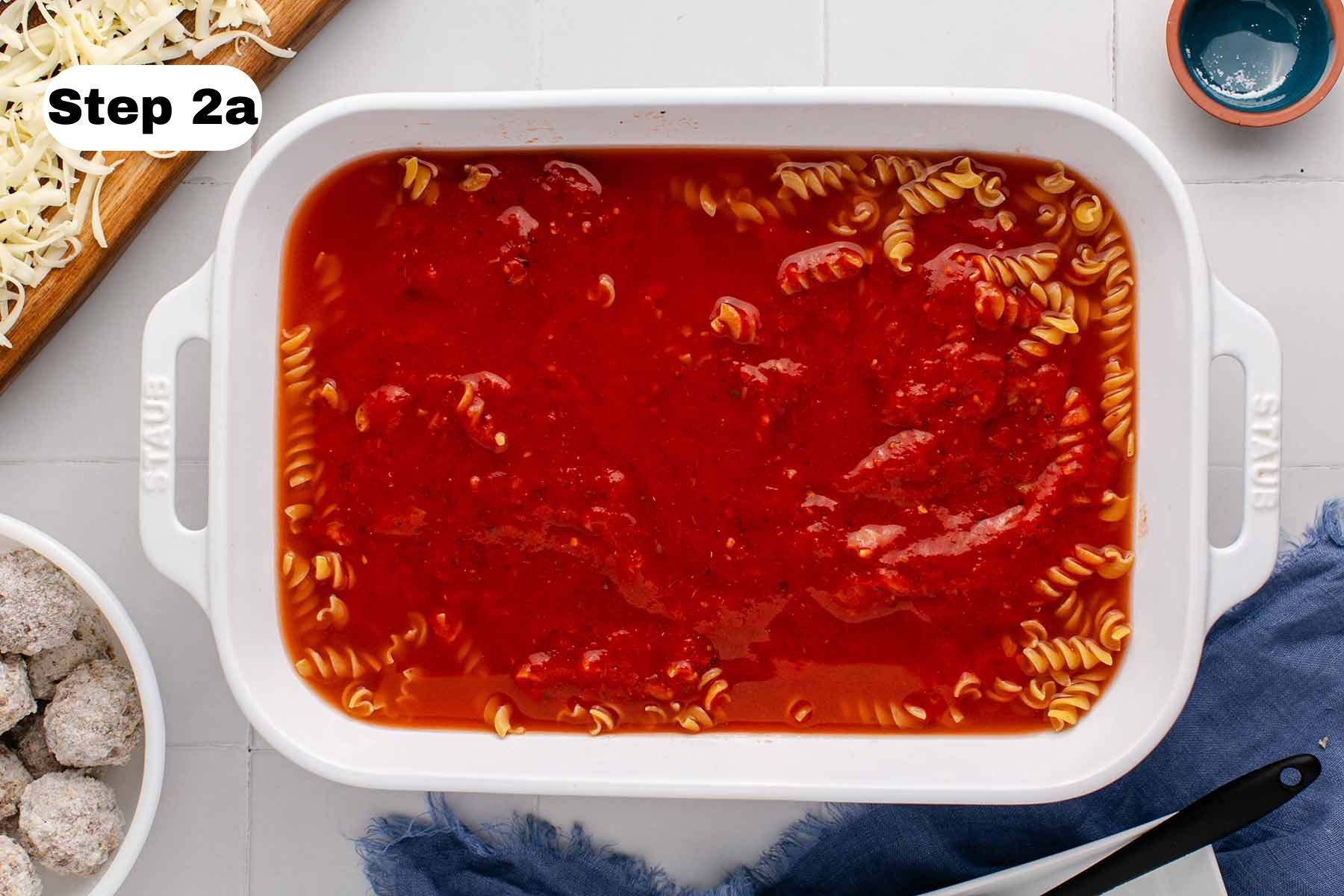 Uncooked rotini pasta and marinara sauce in a large white baking dish.