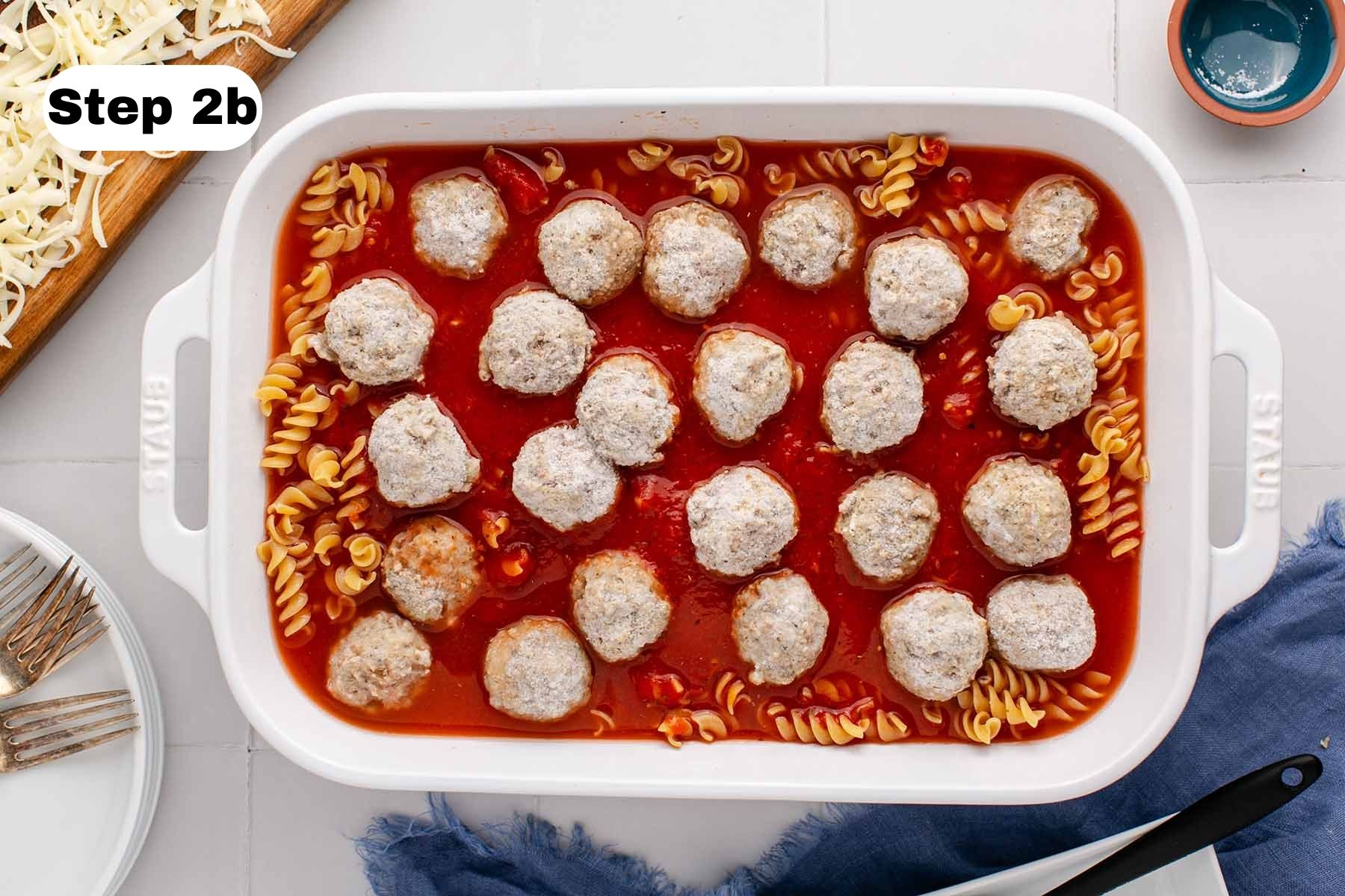 Frozen meatballs sitting on top of pasta and marinara sauce in a large white baking dish