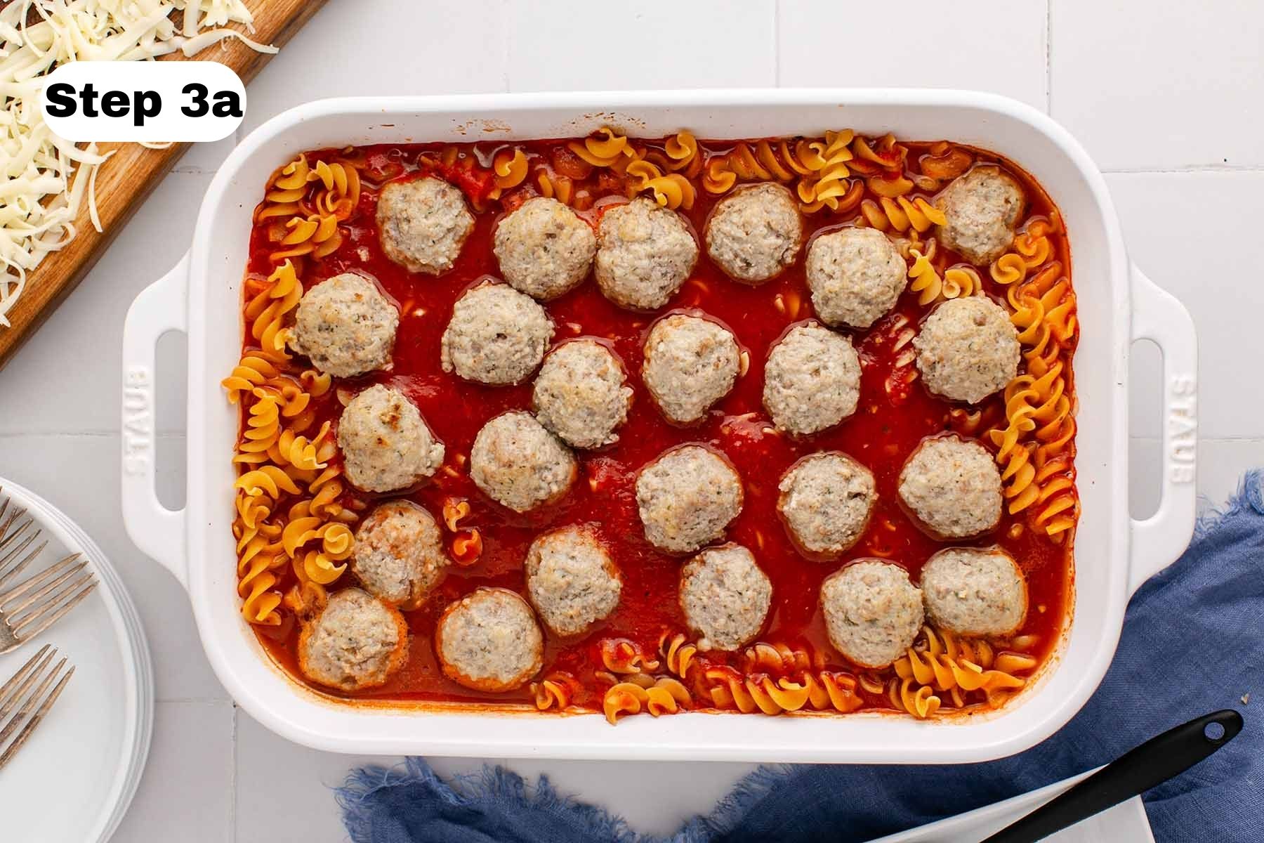 Cooked meatballs, pasta, and marinara sauce in a large white baking dish.