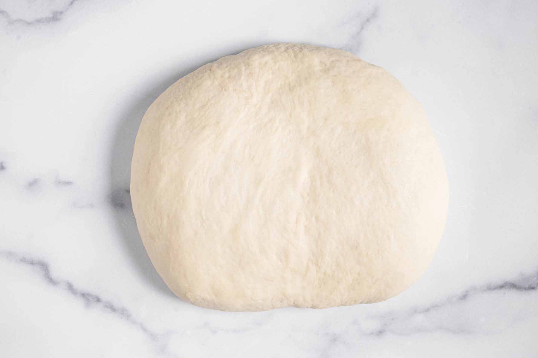 Ball of pizza dough on a marble surface.