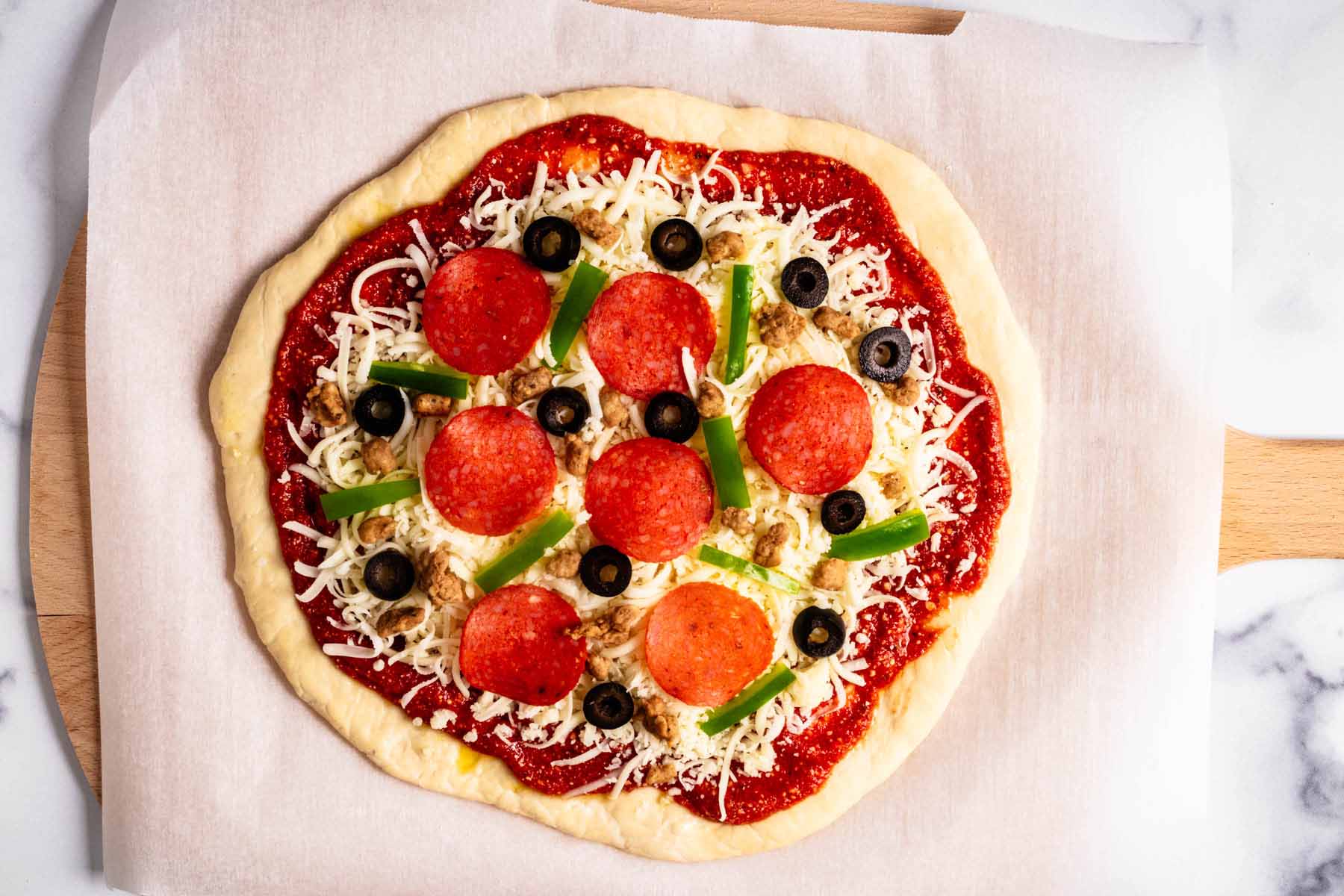 Unbaked pizza on a parchment lined pizza peel