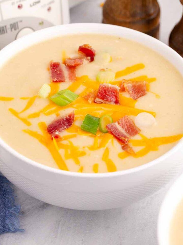 Potato soup topped with bacon bits, grated cheddar cheese, and sliced green onions in a white bowl.