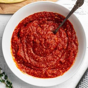 Overhead close up of pizza sauce in a white bowl with a spoon.